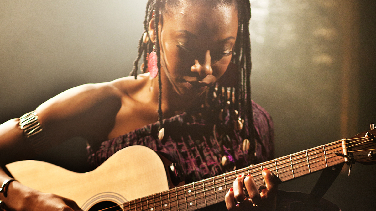 Fatoumata "Fatou" Diawara plays the acoustic guitar bathed in the glow of a spotlight.